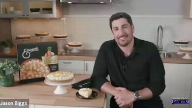 Jason Biggs smiles on a kitchen set with pies on table next to him